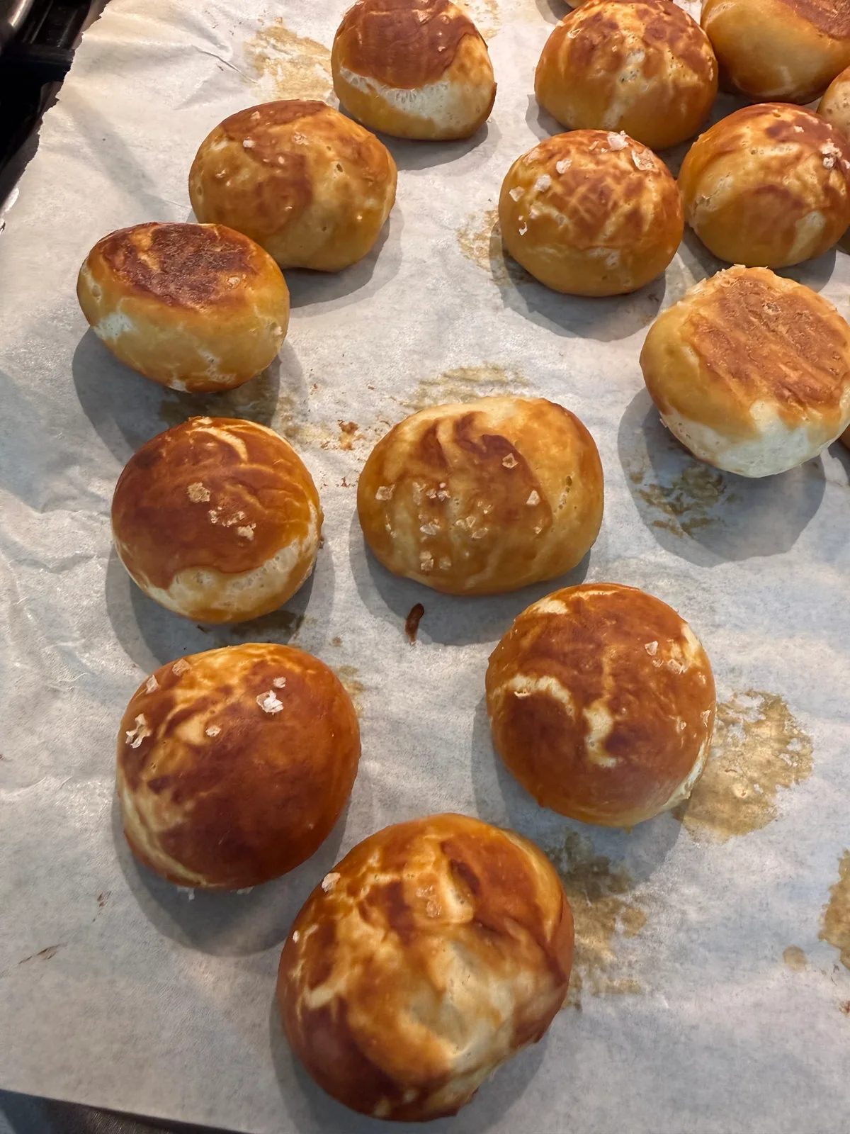 Round golden-brown rolls with glossy, cracked tops and scattered salt flakes on a parchment-lined baking tray.