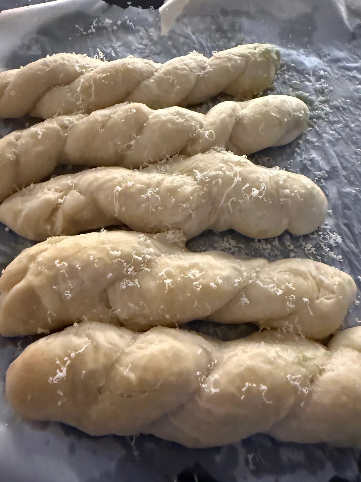 Five pale twisted bread ropes sprinkled with fine white shavings on a parchment-lined baking tray.