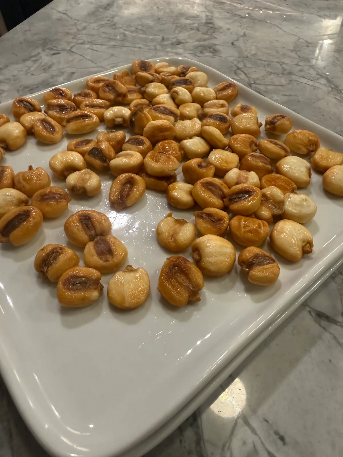 Golden, puffed kernels with browned centers scattered across a large white rectangular platter on a gray marble countertop.